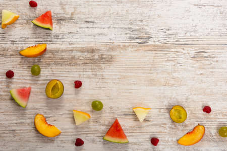Slices of fruit, peach, melon, watermelon, grapes, plum, raspberry, fruit on wooden background. Flat top view, place for text. Flat Lay, Copy Space. Summer background.の写真素材