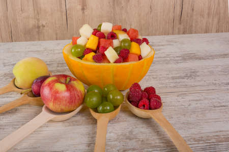 Fruit salad. Peach, watermelon, melon, raspberry, plum, grapes, diced salad Whole fruits in wooden spoons. Place for text. Copy spaceの写真素材