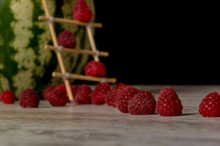 Watermelon house for raspberries. Ladder of chopsticks. Close-up, black background, isolated, place for text.の写真素材