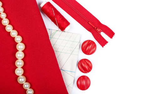Sewing and needlework. Red fabric, threads, buttons, zip fastener and template on a white...