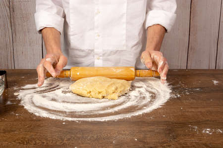 Dough preparation for cookies, pies, cakes, pizza. Hands rolling out on the wooden table, in the...
