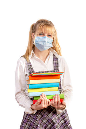 Protection against schoolboy infection during the period of the virus. A high school student with a medical mask on her face holds a stack of textbooks and notebooks on a white isolated background.の写真素材