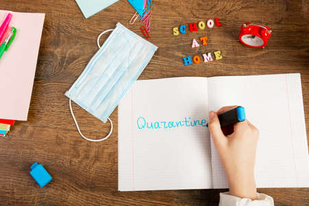 A schoolgirl writes the word "Quarantine" with a marker in a notebook. School at home during the quarantine period. Desk with school accessories, top view, Flat Lay, close-upの写真素材