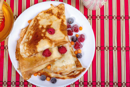 A plate with fried pancakes folded by triangles stands on a bamboo red and white stand. Flat Lay,...