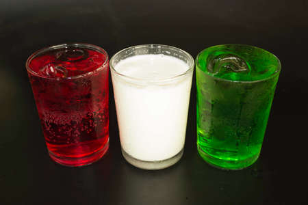 Red and green milk and ice in a glass on a black background.の写真素材