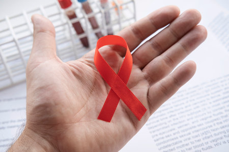 Red ribbon in hand, symbol of fight against AIDS and HIV, conceptual imageの写真素材