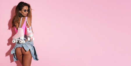 Beautiful young woman with roller skates on pink background, copy spaceの写真素材