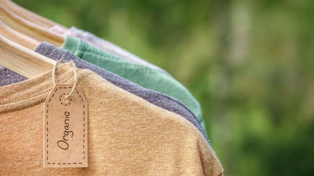 Organic clothes. Natural colored t-shirts hanging on wooden hangers in a row. Eco textile tag. Green...
