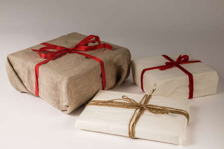 Christmas gift boxes on white background. Burlap canvas and organic white reused / recycled wrapping paper. Red ribbon and natural linen string.の写真素材