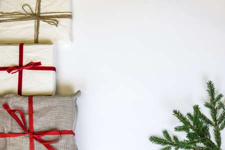 Christmas gift boxes on white background. Burlap canvas and organic white reused / recycled wrapping paper. Red ribbon and natural linen string. Fir twig. Empty blank copy space for text.の写真素材