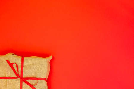 Christmas gift box on red background. Burlap canvas wrapping textile with red ribbon. Empty blank copy space for text.の写真素材