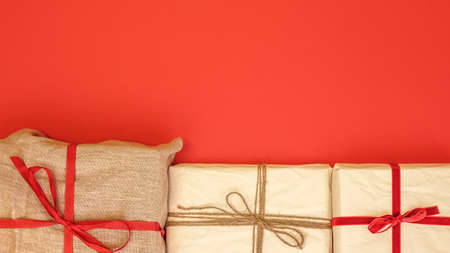 Christmas gift boxes on red background. Burlap canvas and reused wrapping paper with red ribbon and linen string. Empty blank copy space for text.の写真素材