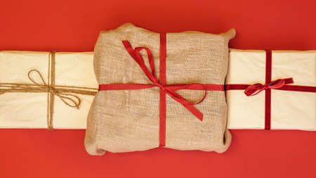 Christmas gift boxes on red background. Burlap canvas and reused wrapping paper with red ribbon and linen string.の写真素材
