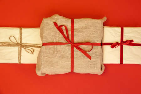 Christmas gift boxes on red background. Burlap canvas and reused wrapping paper with red ribbon and linen string.の写真素材