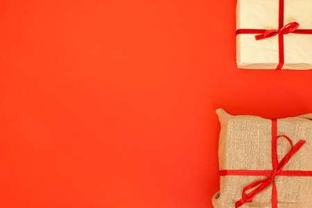 Christmas gift boxes on red background. Burlap canvas and reused wrapping paper with red ribbon and linen string. Empty blank copy space for text.の写真素材