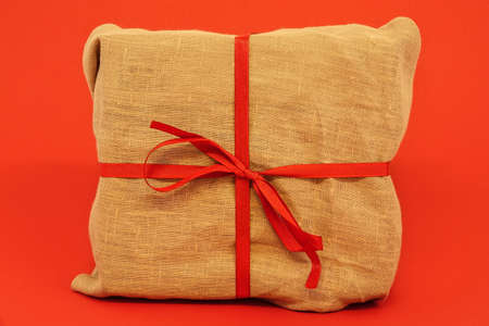 Christmas gift box on red background. Burlap canvas wrapping textile with red ribbon.の写真素材