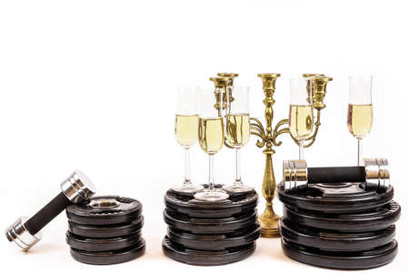 New Year Resolution. Celebrate new years eve at the gym. Glasses of champagne on weight plates and dumbbells. Workout and exercise more next year. Empty copy space on white background.の写真素材