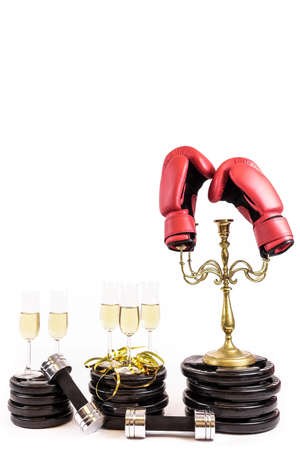 New Year Resolution. Celebrate new years eve at the gym. Glasses of champagne on weight plates and dumbbells. Boxing gloves on candelabra. Workout and exercise more next year. Empty copy space for text on white background.の写真素材