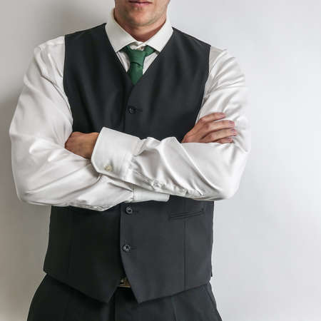 Businessman in black waistcoat vest, white shirt and a tie with his arms crossed. White background.の写真素材