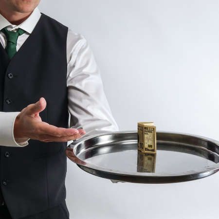 Butler / waiter holds a silver tray with a ten dollar bill. Concept for tip and money exchange. White background.の写真素材