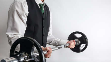 Businessman in white shirt and black suit vest performing biceps curl with EZ curl bar. Concept for new year resolution and workout, exercise at work / office. Copy space on white background.の写真素材