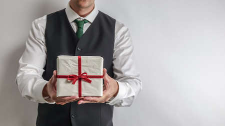 Businessman in white shirt and black suit vest holding a Christmas gift / present. Copy space for text on white background.の写真素材