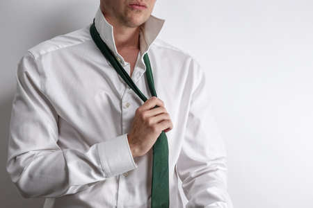 Well dressed man in white shirt get dressed / undressed. Shirt collar unfold and corrects his tie. White background with copy space for text.の写真素材