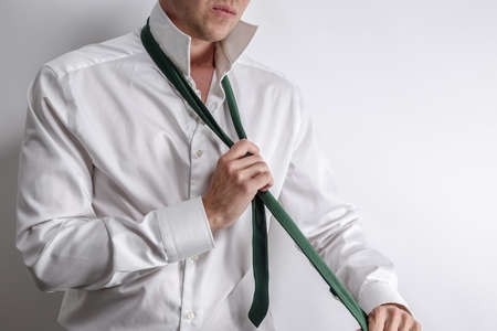 Well dressed man in white shirt get dressed / undressed. Shirt collar unfold and take off his tie. White background with copy space for text.の写真素材