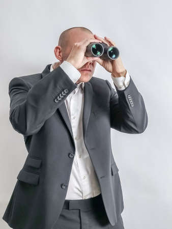 Businessman in white shirt and black suit scouts in binoculars. Concept for job search and long term unemployment, LTU.の写真素材