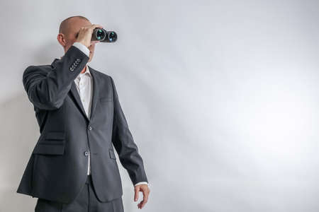 Businessman in white shirt and black suit scouts in binoculars. Concept for job search and long term unemployment, LTU. White background with copy space for text.の写真素材