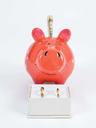 Wedding became more expensive than expected.Piggy bank smiling behind box with wedding rings. Vertical.の写真素材