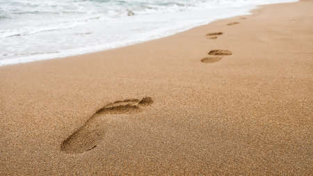 Close up of footprints in wet sand on the beach at sunset. Concept for traveling to tropical / exotic places, vacation and holiday.の写真素材