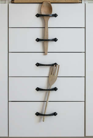 Simple homemade child safety for kitchen cabinets. A wooden spoon and fork inserted between the handles on the drawers.の写真素材