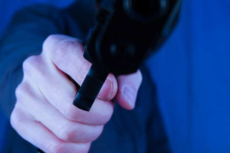 A robber / criminal aiming with a gun. Assault with deadly weapon. Blueish cold scary picture.