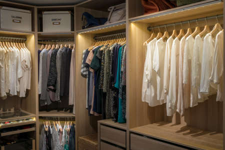 Luxury walk in closet / dressing room with lighting and jewel display. Dresses, handbags, blouses and sweaters on hangers in the wardrobes. Hoizontal.の写真素材