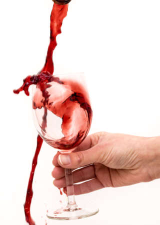 Red wine is poured into a glass held by a hand. Spill wine wildly. Artistic beautiful picture.の写真素材