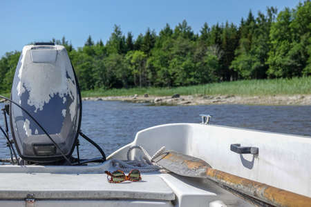 Boat with old tired outboard engine. Oars, sunglasses and rope. Concept for fishing, vacation and weekend.の写真素材