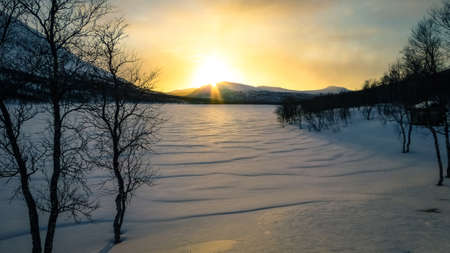 Sunset over a frozen snowy lake in the mountains of northern Sweden near the polar circle.の写真素材