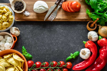 Ingredients for Italian food. Fresh vegetables, mozzarella cheese, herbs and pasta on dark stone background.の写真素材