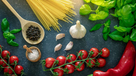 Italian food cooking ingredients. Tomatoes, spaghetti pasta, basil, garlic and seasoning spices on dark stone background.の写真素材
