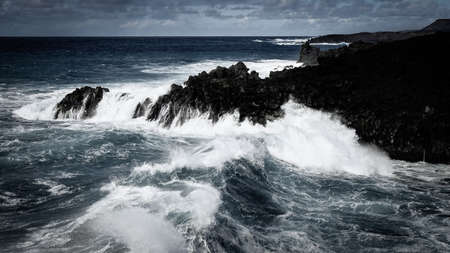 Waves crash along the black lava rock cliffs. Lanzarote, Canary Islands.の写真素材