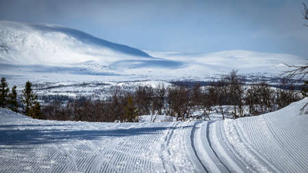 Cross country skiing. Empty touring ski trail. Snowy mountains in the background.の写真素材