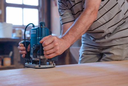 male person working with carpentry hand power tools in the manufacture of a wooden table. Handcrafted carpenter's manual laborの写真素材