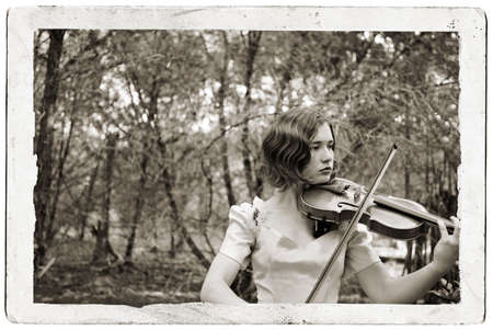 Monotone photo of pretty girl in an antique party dress playing the violin in the woods composited...