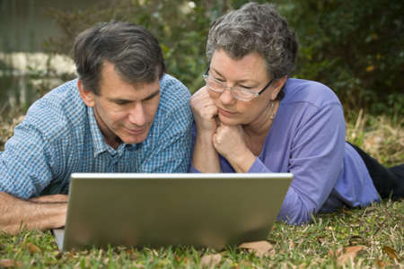 Attractive senior couple working together on the computer in an outdoor setting.