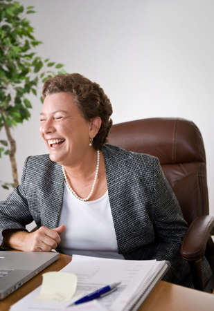 Mature woman at her desk in an office laughing uproariously.の写真素材