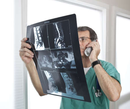Doctor looking at radiology scan. Short depth of field. Focus on MRI/Xray film. Doctor out of focus.の写真素材