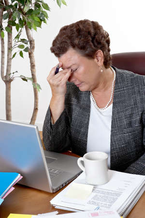 Mature business woman at her desk, eyes closed, worried about bills and financial problems