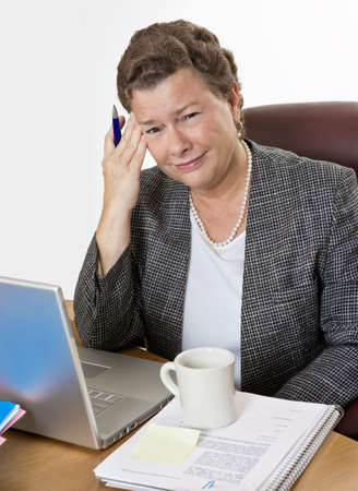 Mature businesswoman at her desk having a hot flash and a headache, looking at camera, very distressed.の写真素材