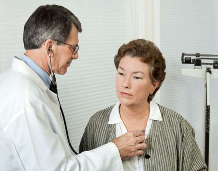 Male doctor listens to mature woman's heart during an office visit.の写真素材